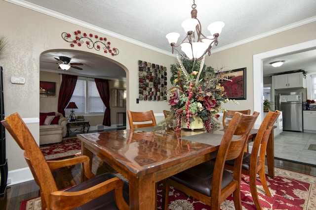 dining space with arched walkways, a textured ceiling, ornamental molding, and ceiling fan with notable chandelier