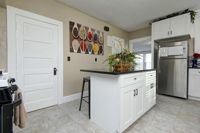 kitchen with a kitchen island, freestanding refrigerator, white cabinetry, dark countertops, and a kitchen bar