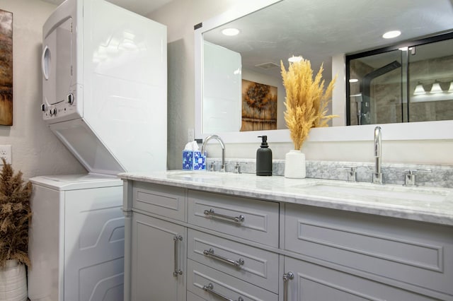 bathroom with a sink, visible vents, stacked washer and dryer, and double vanity