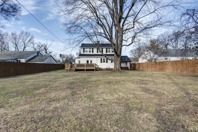 rear view of property featuring a lawn, a deck, a fenced backyard, a shingled roof, and a chimney