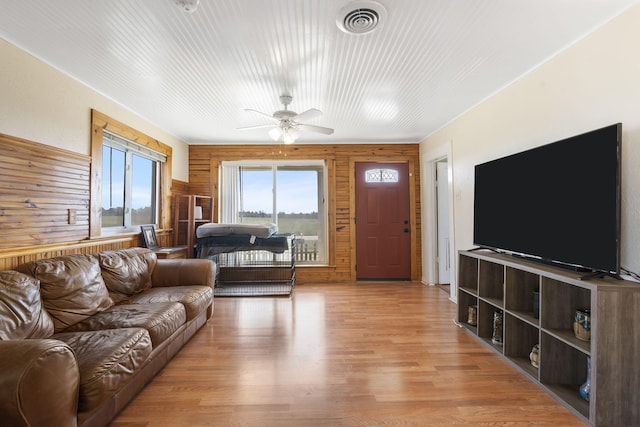 living area featuring visible vents, wood walls, light wood-type flooring, and a ceiling fan