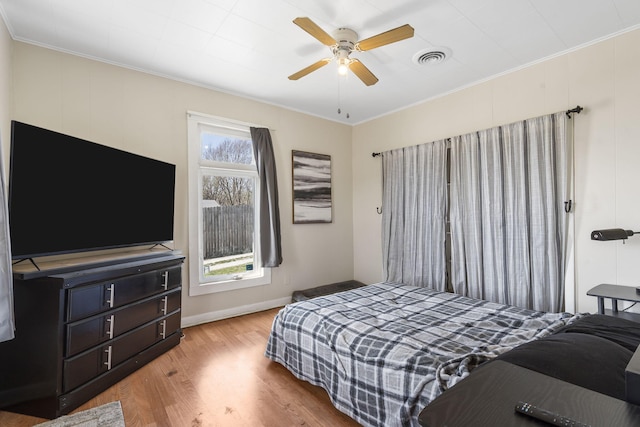 bedroom with visible vents, a ceiling fan, crown molding, light wood finished floors, and baseboards