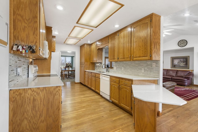 kitchen with a sink, white appliances, light wood finished floors, light countertops, and vaulted ceiling