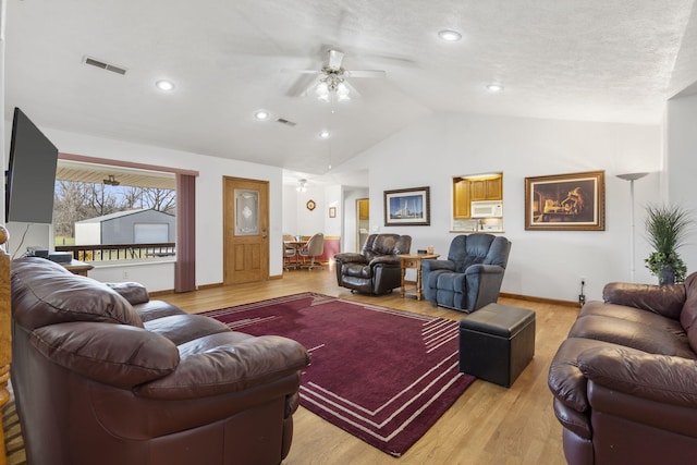 living room featuring visible vents, ceiling fan, lofted ceiling, light wood-style floors, and a textured ceiling