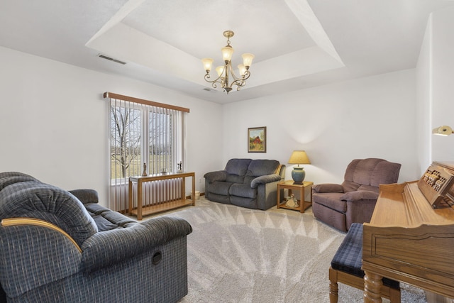 living room featuring a tray ceiling, visible vents, carpet floors, and a chandelier