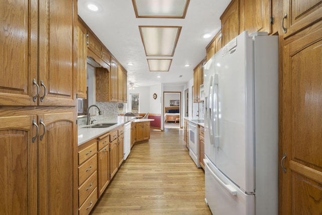 kitchen featuring a sink, white appliances, brown cabinetry, and light wood finished floors