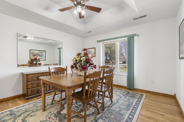 dining space with a tray ceiling, visible vents, light wood-style floors, and a ceiling fan