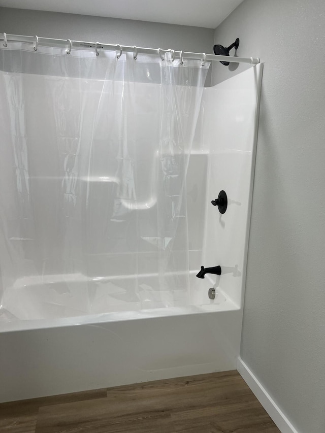 bathroom featuring wood finished floors, baseboards, and shower / tub combo with curtain