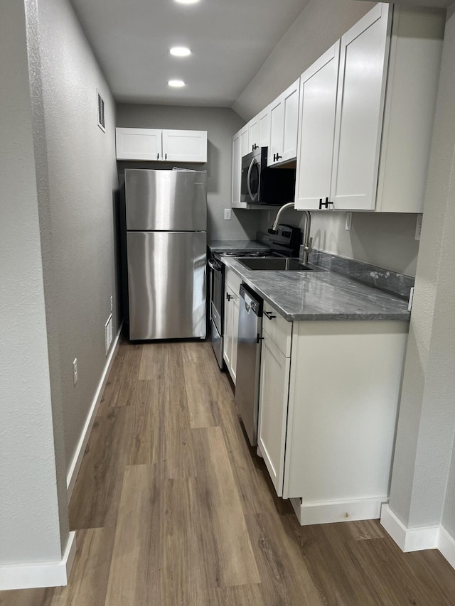 kitchen featuring wood finished floors, appliances with stainless steel finishes, white cabinetry, and a sink