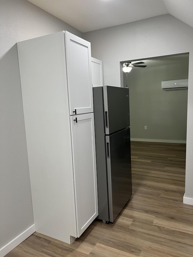 kitchen featuring a wall mounted air conditioner, wood finished floors, freestanding refrigerator, white cabinets, and baseboards