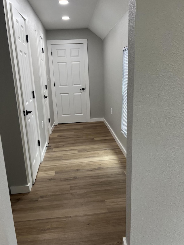 corridor with vaulted ceiling, baseboards, and wood finished floors