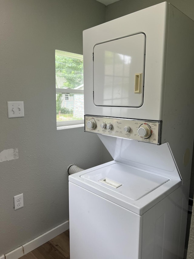 laundry area featuring laundry area, stacked washing maching and dryer, baseboards, and wood finished floors