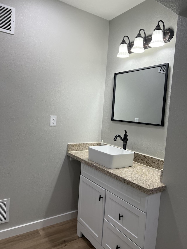 bathroom with visible vents, vanity, baseboards, and wood finished floors