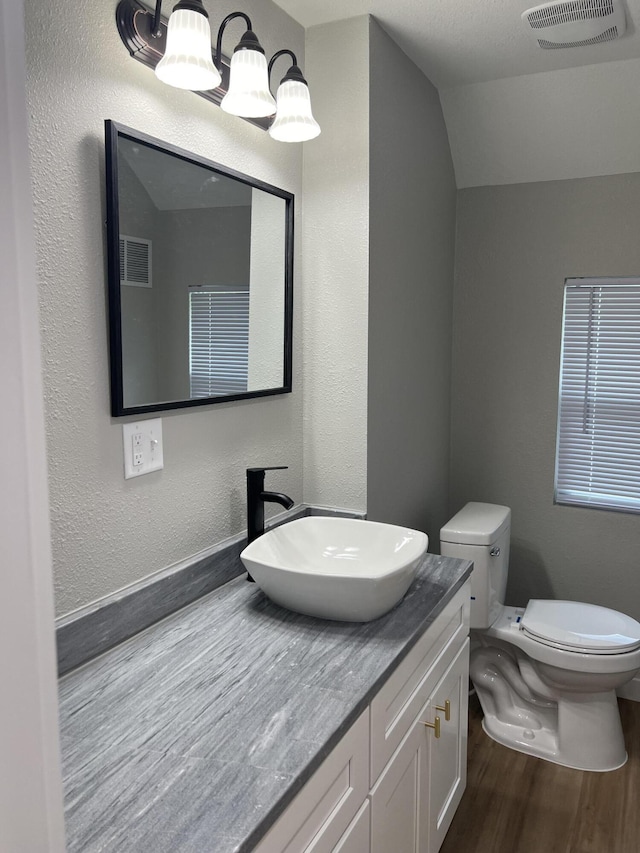 half bathroom with visible vents, toilet, wood finished floors, and vanity