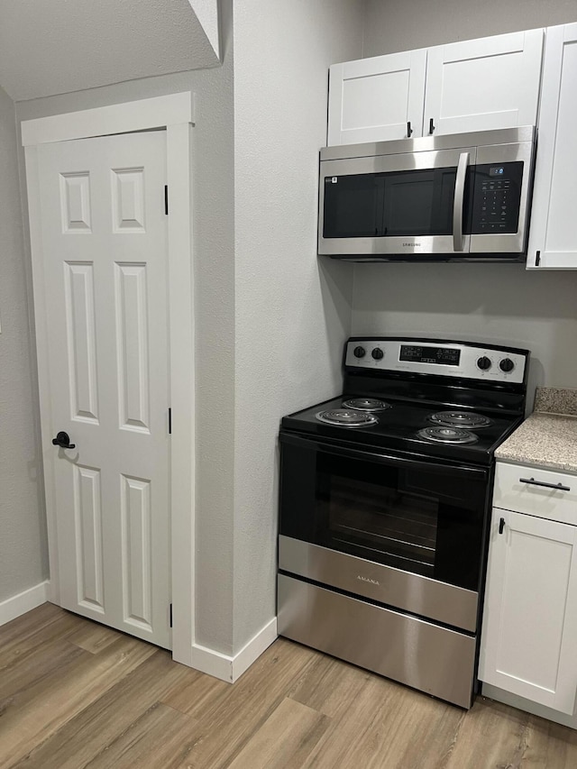 kitchen with white cabinets, appliances with stainless steel finishes, baseboards, and light wood-style floors