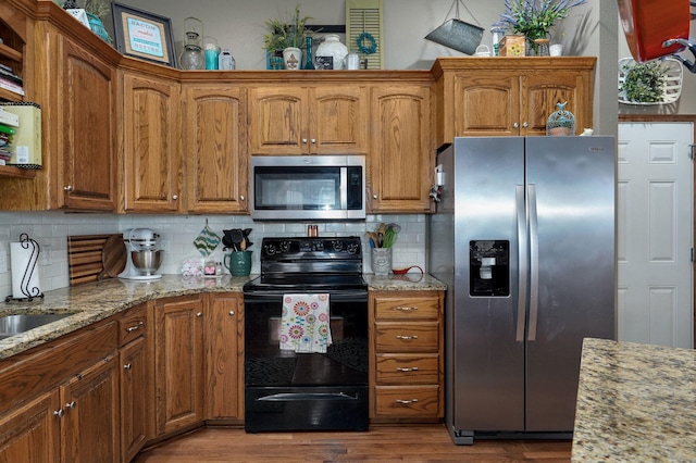 kitchen featuring light stone counters, wood finished floors, appliances with stainless steel finishes, brown cabinetry, and decorative backsplash