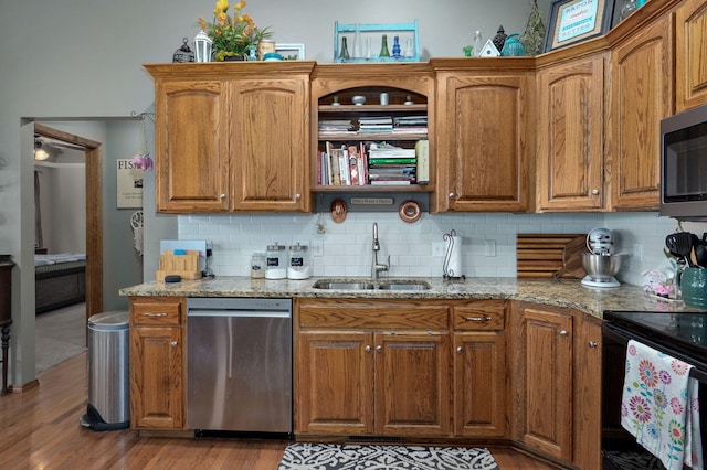 kitchen with a sink, light wood-type flooring, light stone counters, and appliances with stainless steel finishes