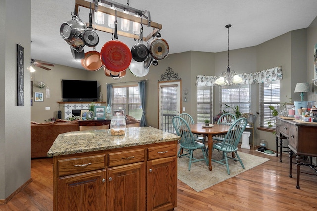 kitchen featuring light wood finished floors, baseboards, light stone countertops, ceiling fan with notable chandelier, and brown cabinets