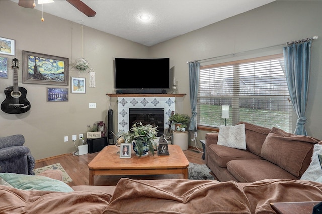 living area featuring a tiled fireplace, vaulted ceiling, a ceiling fan, and wood finished floors