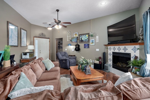 living area featuring a tiled fireplace, ceiling fan, and wood finished floors