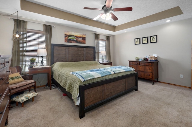 bedroom featuring a raised ceiling, multiple windows, light colored carpet, and baseboards