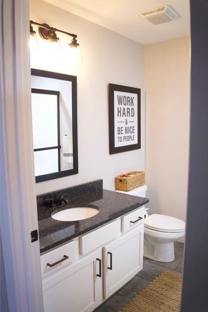 half bath with vanity, toilet, and visible vents