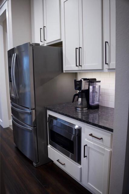 kitchen featuring backsplash, dark wood-type flooring, dark stone counters, appliances with stainless steel finishes, and white cabinetry