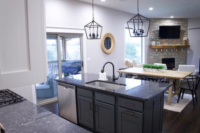 kitchen featuring dark wood finished floors, a sink, dark stone counters, and stainless steel dishwasher