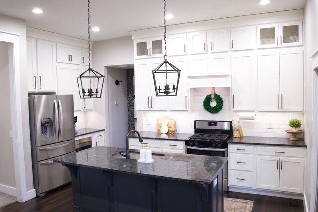 kitchen with a kitchen island with sink, a sink, stainless steel appliances, dark stone counters, and glass insert cabinets