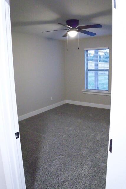 empty room featuring dark carpet, baseboards, and ceiling fan