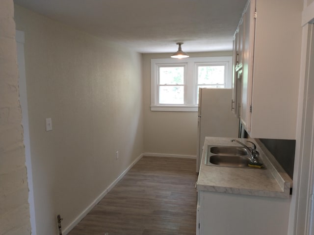 kitchen with white cabinetry, light countertops, baseboards, and a sink