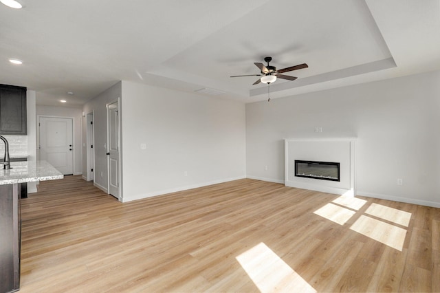 unfurnished living room featuring baseboards, a raised ceiling, light wood-style floors, and ceiling fan