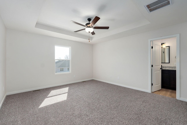 unfurnished bedroom with a tray ceiling, visible vents, baseboards, and light colored carpet