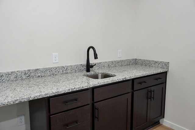 kitchen featuring light stone counters, baseboards, light wood finished floors, a sink, and dark brown cabinetry