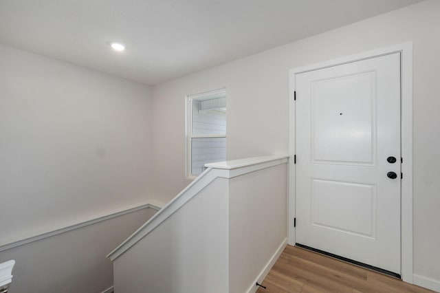 hall featuring an upstairs landing, light wood-type flooring, and baseboards