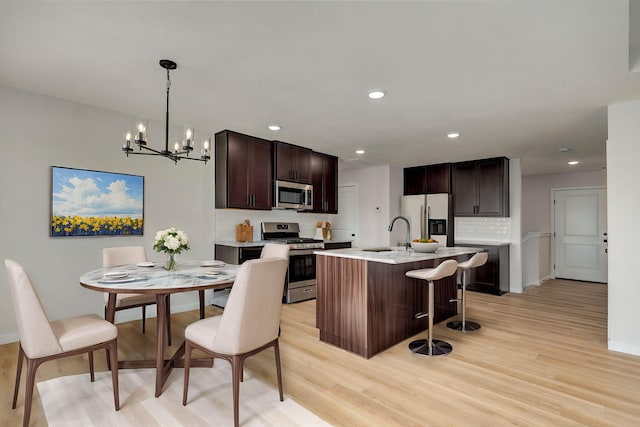 kitchen with backsplash, appliances with stainless steel finishes, a kitchen breakfast bar, an inviting chandelier, and a sink