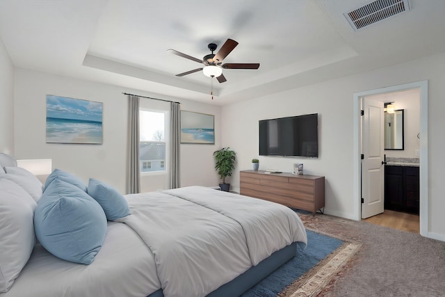 bedroom with visible vents, light carpet, ensuite bathroom, a tray ceiling, and baseboards