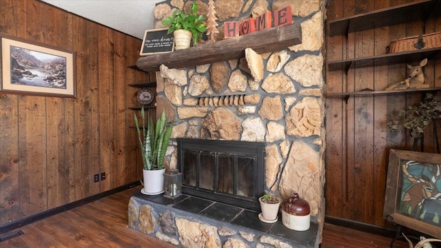 details with visible vents, wood finished floors, wooden walls, a stone fireplace, and baseboards