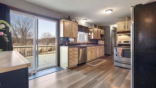 kitchen featuring light brown cabinetry, under cabinet range hood, wood finished floors, stainless steel appliances, and a sink