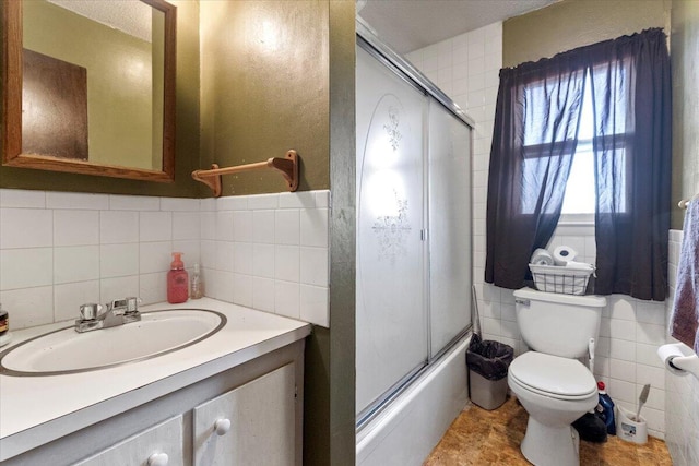 full bath featuring combined bath / shower with glass door, toilet, tile walls, and vanity