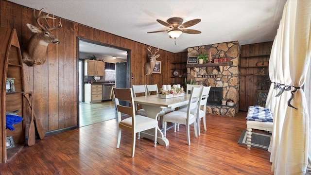 dining area featuring ceiling fan, wood finished floors, wood walls, and a fireplace