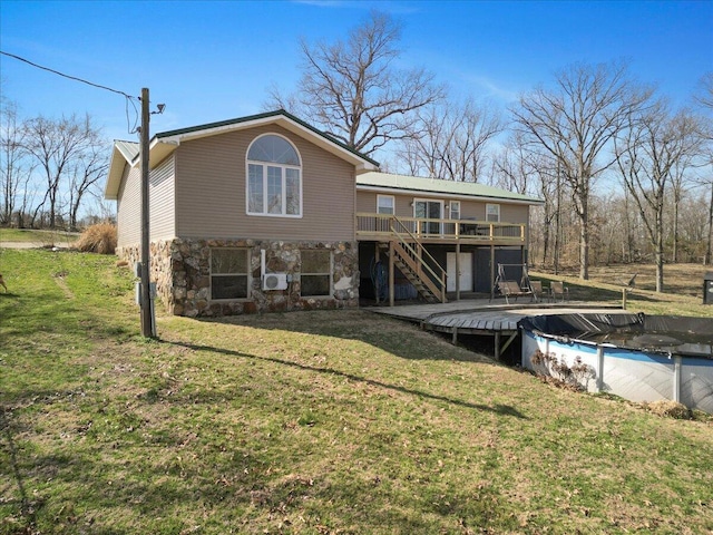 rear view of house featuring stairway, a covered pool, stone siding, a deck, and a lawn