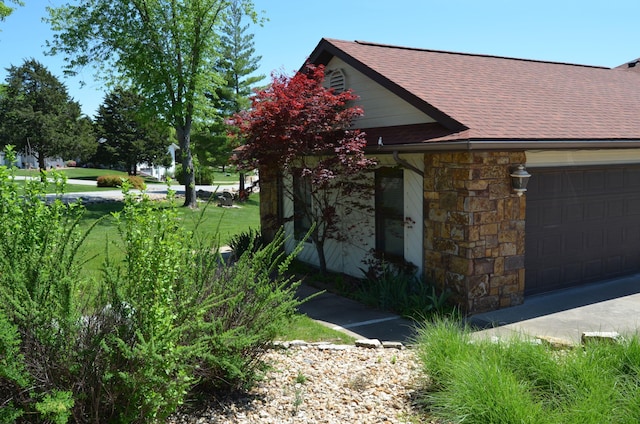 view of side of home with an attached garage, roof with shingles, and stone siding