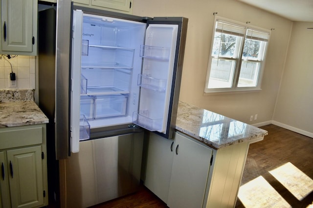 kitchen with light stone counters, baseboards, dark wood finished floors, freestanding refrigerator, and backsplash