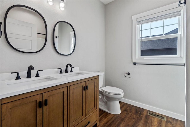 bathroom with toilet, wood finished floors, visible vents, and a sink