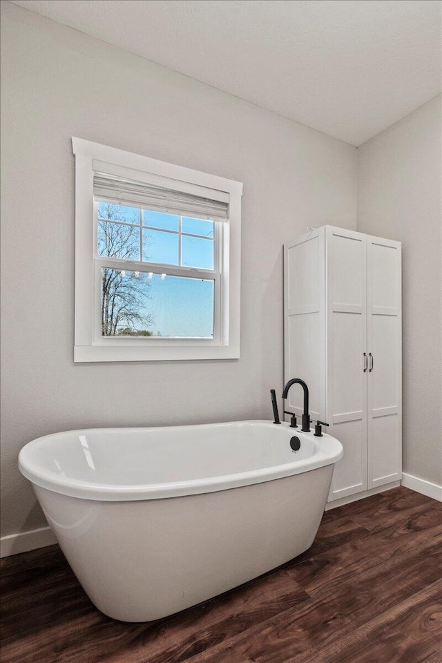 bathroom featuring a freestanding tub, baseboards, and wood finished floors