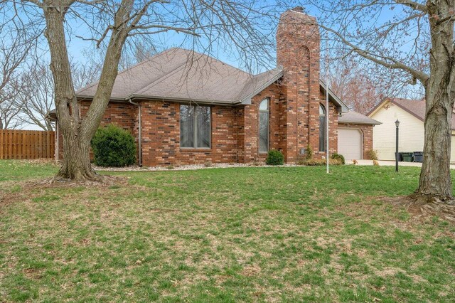 view of front of property featuring brick siding, fence, a front yard, a chimney, and a garage