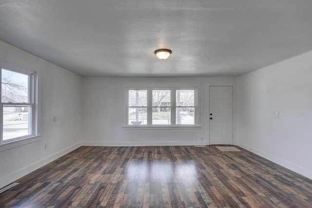 empty room with visible vents, a healthy amount of sunlight, dark wood-type flooring, and baseboards