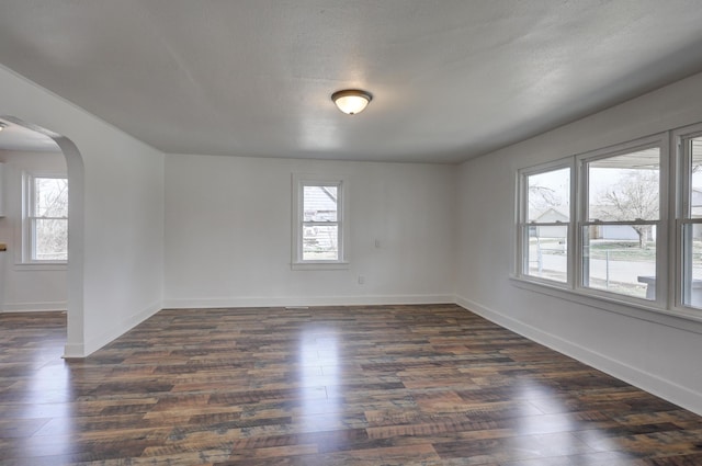 unfurnished room featuring a wealth of natural light, arched walkways, and dark wood-style flooring