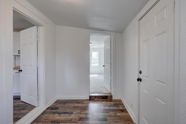 hall featuring baseboards, dark wood-type flooring, and a textured ceiling